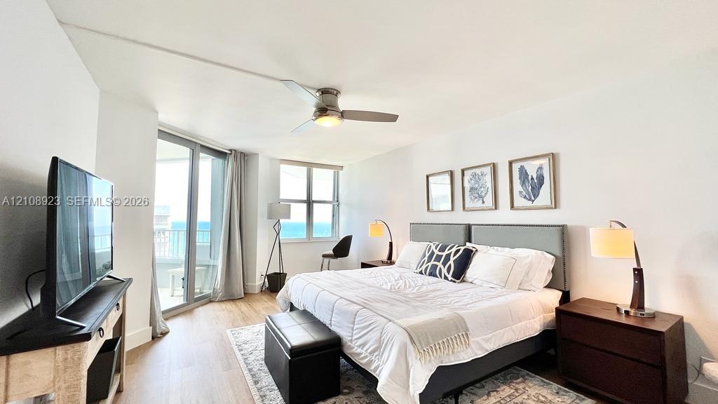 Wood-finish flooring, ceiling fan with integrated lighting, expansive windows, and glass door access to an exterior balcony