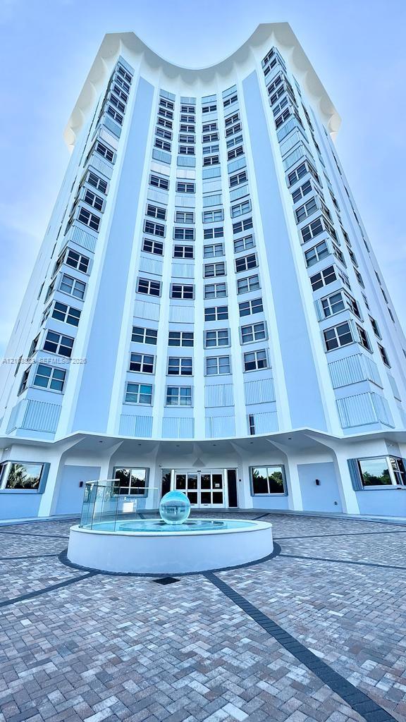 High-rise architectural exterior featuring a distinct curved facade, geometric patterned paver stone drive, and a central spherical fountain