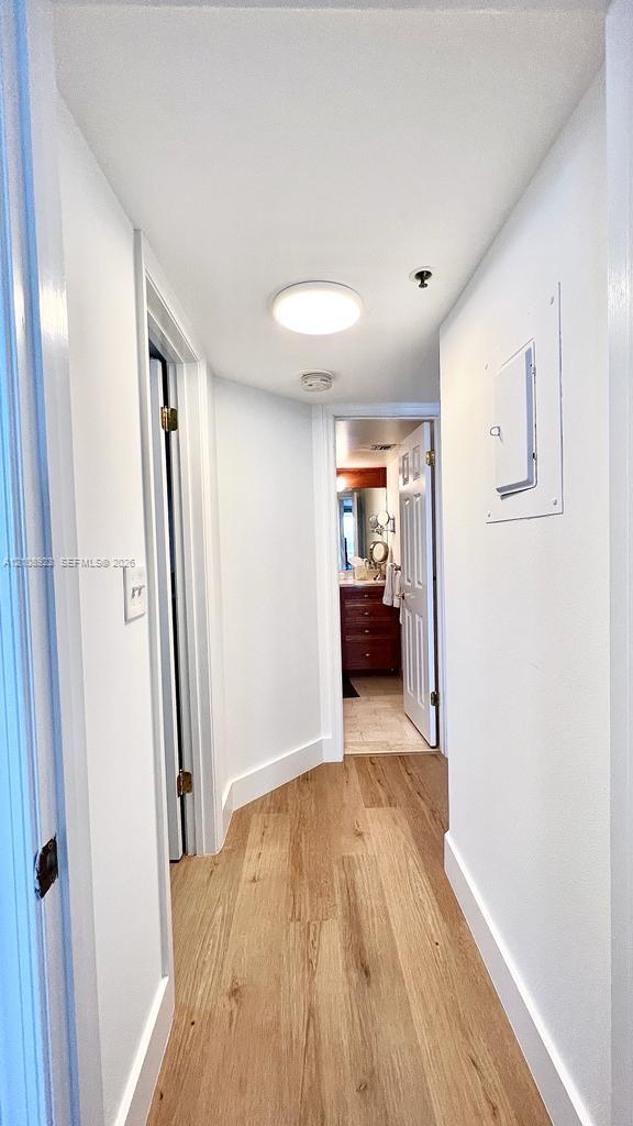 Hallway featuring light-toned wood-finish flooring, crisp neutral paint, and a flush-mount overhead light fixture