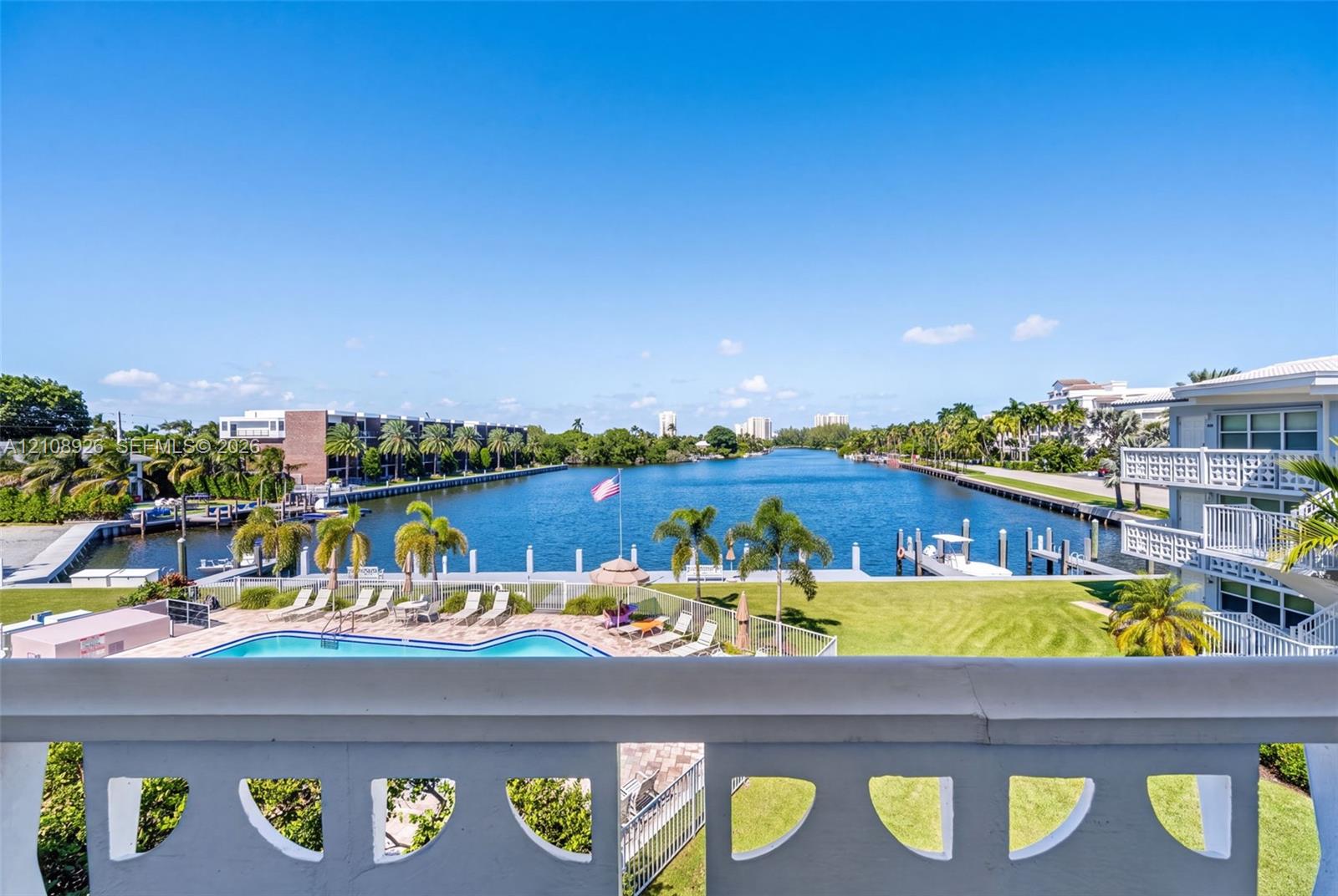 Balcony with white concrete balustrade overlooking a swimming pool, lawn area, and waterway with boat docks