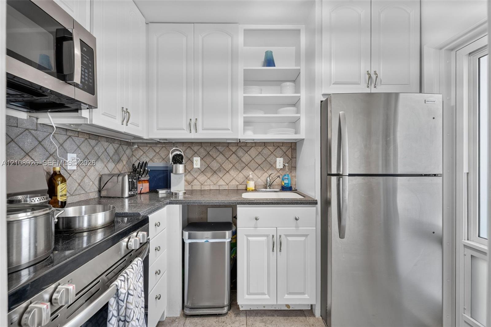 Kitchen featuring white cabinetry, stainless steel appliances, dark stone-finish countertops, open shelving, and a tiled backsplash