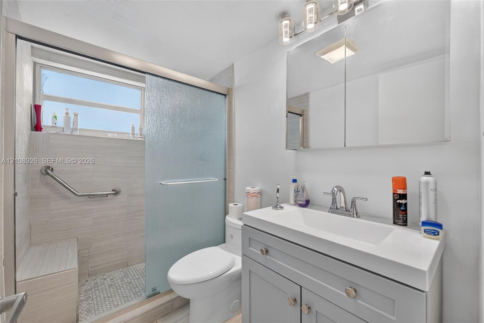 Bathroom featuring a gray vanity with a white integrated sink, walk-in shower with sliding glass doors, horizontal tile wall finishes, and a built-in shower bench