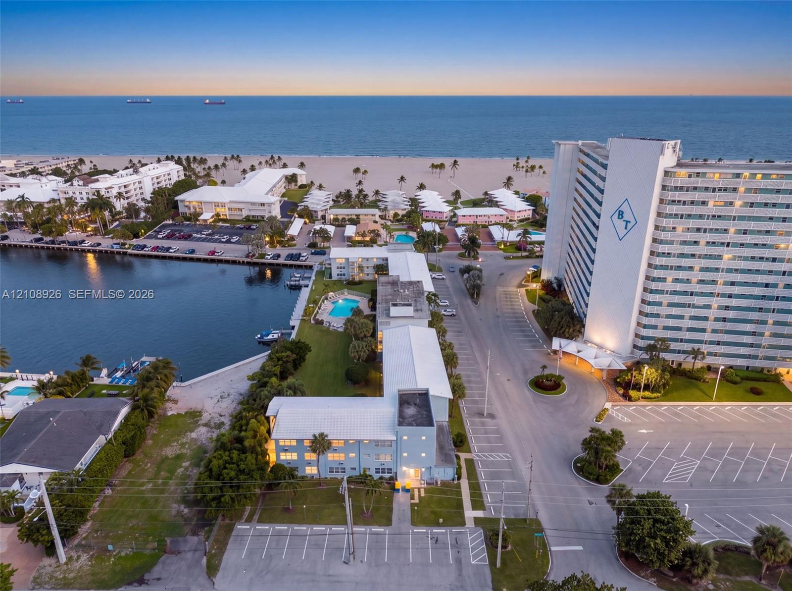 Aerial perspective of property featuring an outdoor swimming pool, direct water frontage, multi-level parking lot, and proximity to the coastline