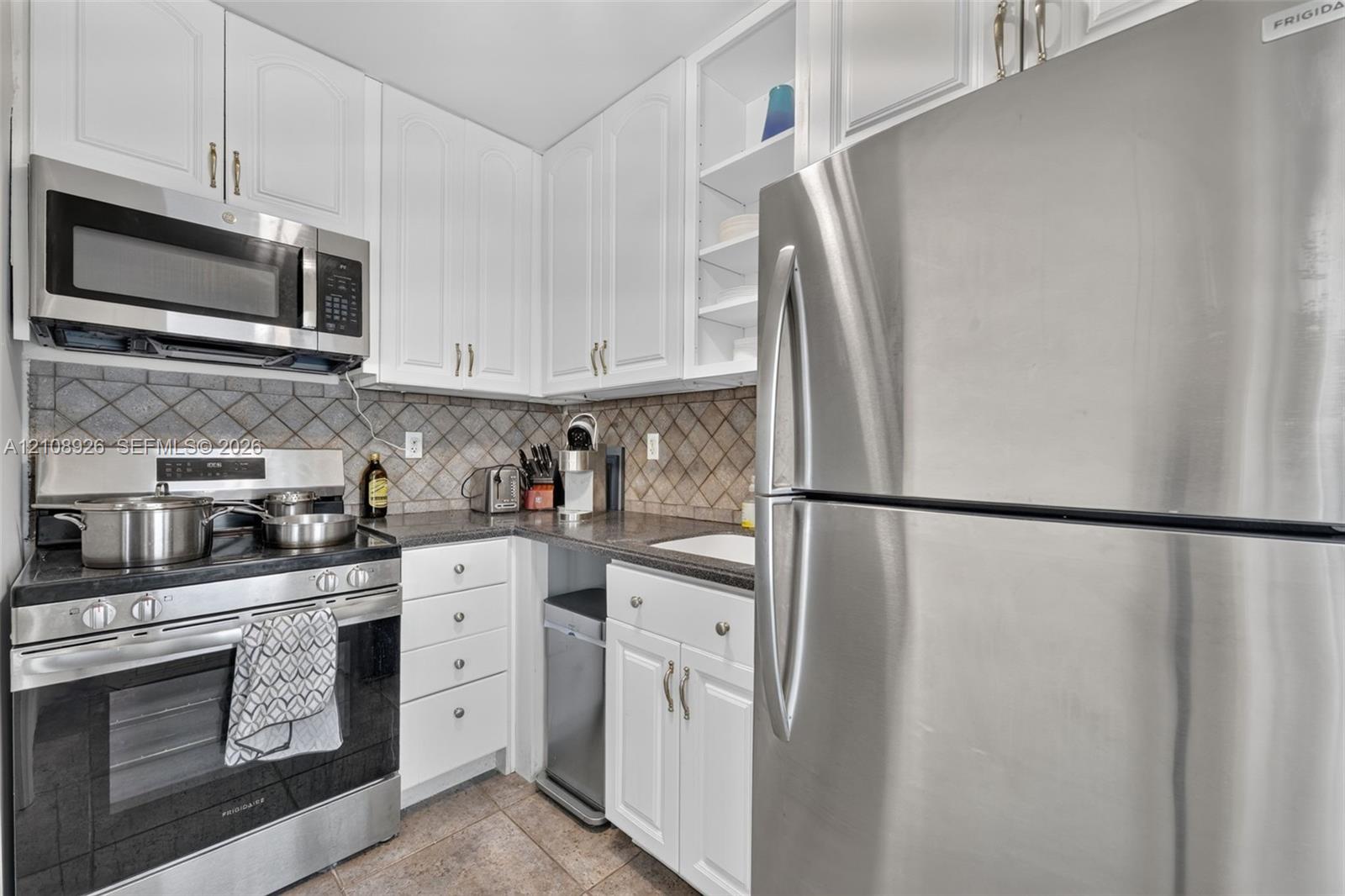 Kitchen featuring white cabinetry, stainless steel appliances, dark stone-finish countertops, ceramic tile backsplash, and tile flooring