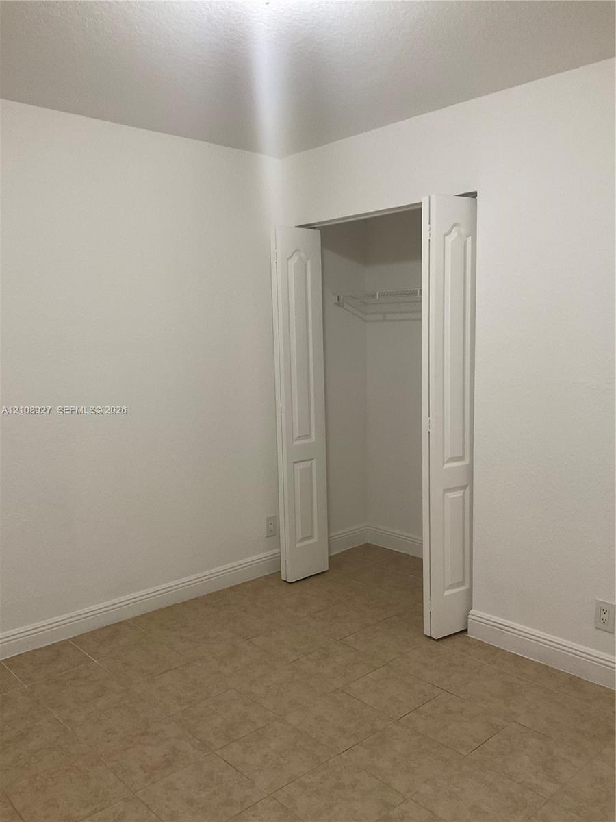 Room featuring neutral wall finishes, tile flooring, and a closet with bifold doors and built-in wire shelving