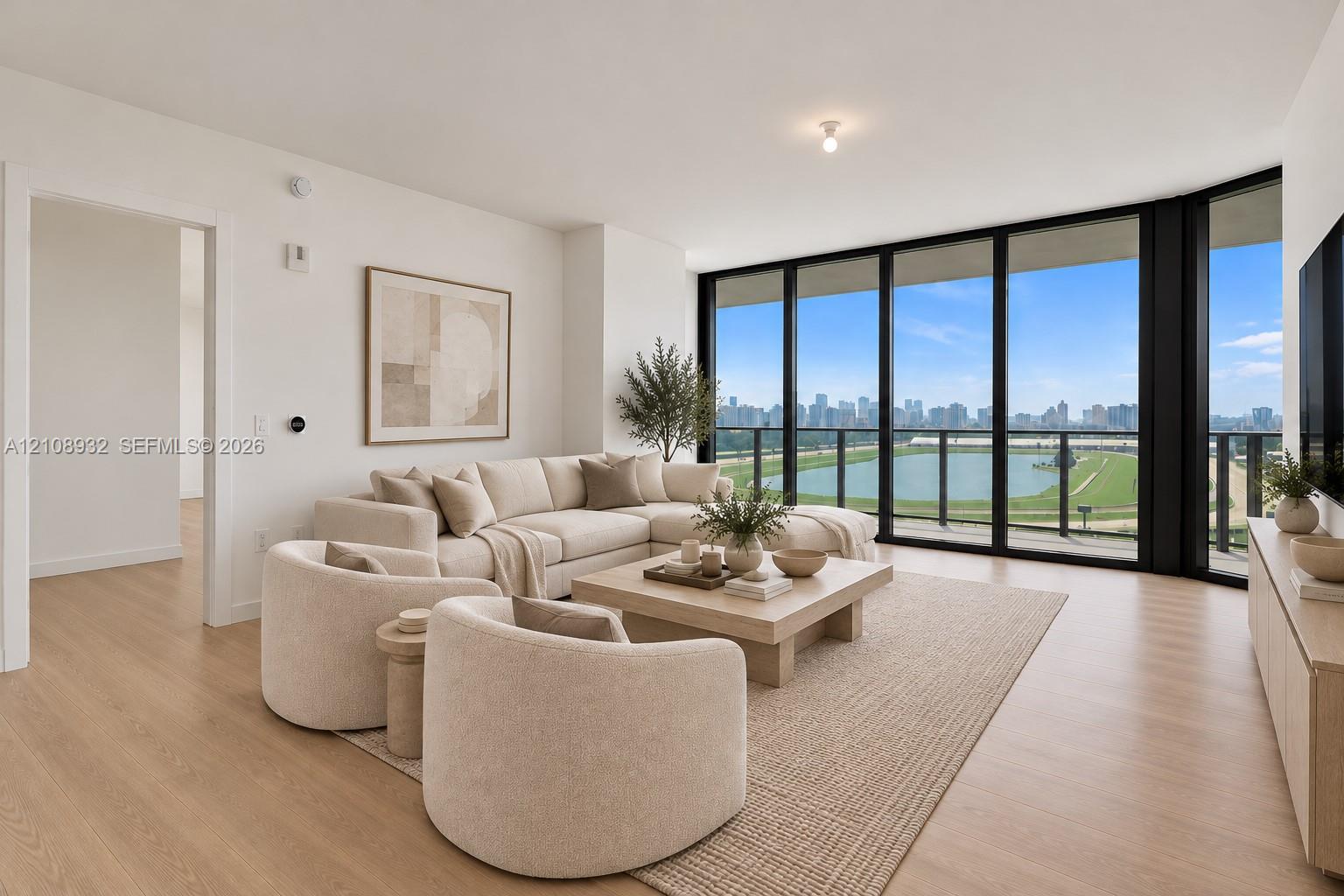 Floor-to-ceiling black-framed windows, wood-finish flooring, and balcony access showcasing water and urban scenery