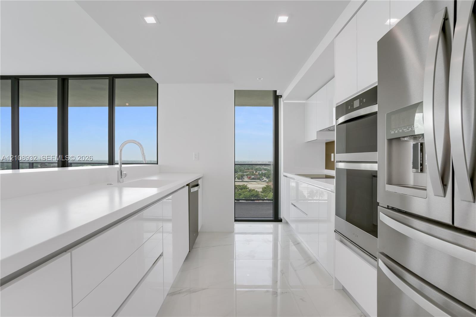 Kitchen featuring white gloss cabinetry, expansive solid-surface countertops, stainless steel double wall ovens, high-gloss tile flooring, and floor-to-ceiling windows