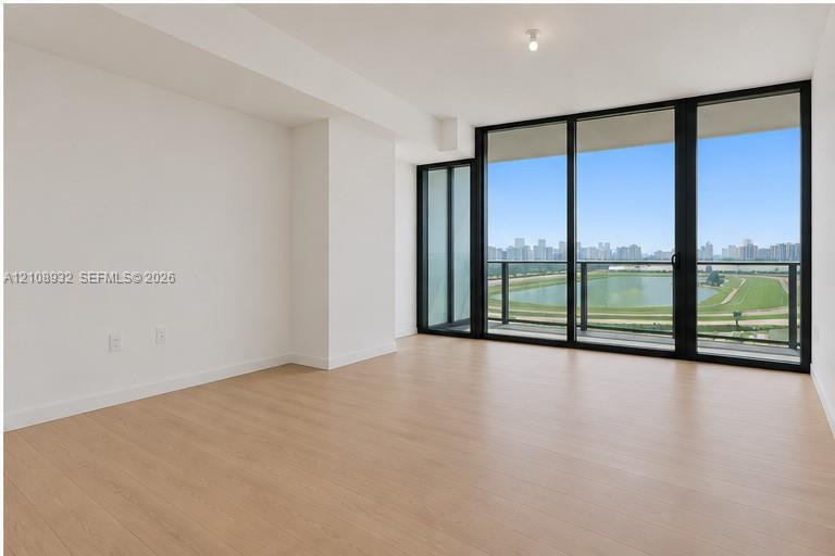Floor-to-ceiling windows, wood-finish flooring, and access to a balcony with metallic railing