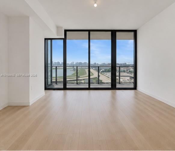 Floor-to-ceiling windows with black frames, wood-finish flooring, and a glass-railing balcony