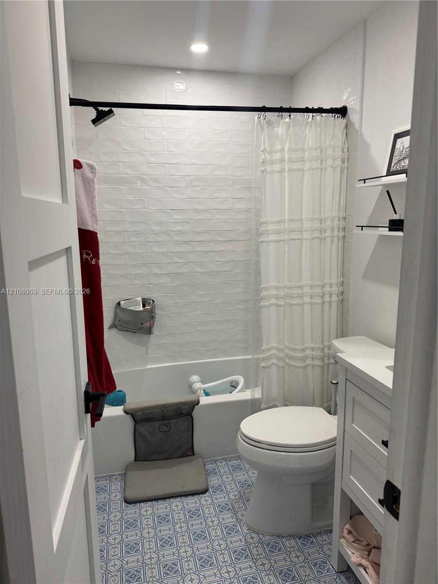 Bathroom featuring patterned floor tile, white subway tile shower surround, recessed ceiling lighting, a white vanity with integrated cabinetry, and matte black hardware