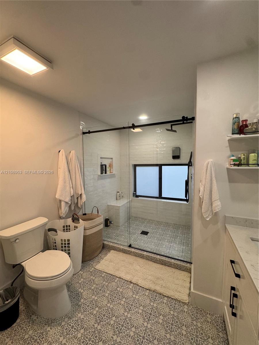Bathroom featuring a walk-in shower with glass enclosure, built-in bench, patterned tile flooring, and stone-top vanity with black hardware
