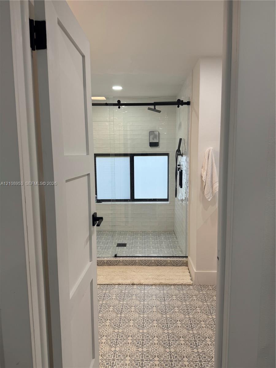 Walk-in shower with patterned tile flooring, white horizontal subway tile wall surround, black sliding glass door hardware, and black plumbing fixtures