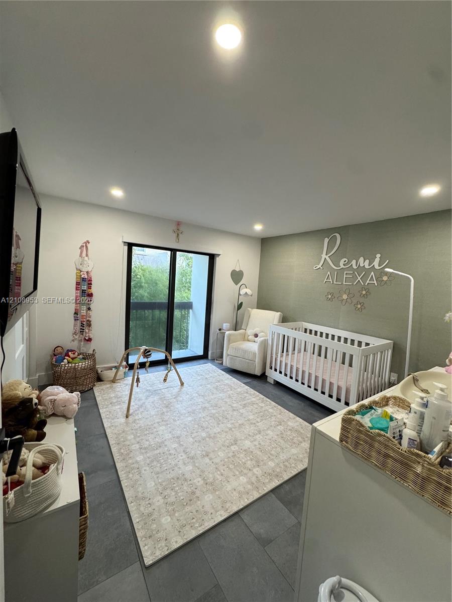 Neutral-toned interior space featuring large-format tile flooring, recessed ceiling lighting, a textured accent wall, and glass sliding doors with black framing