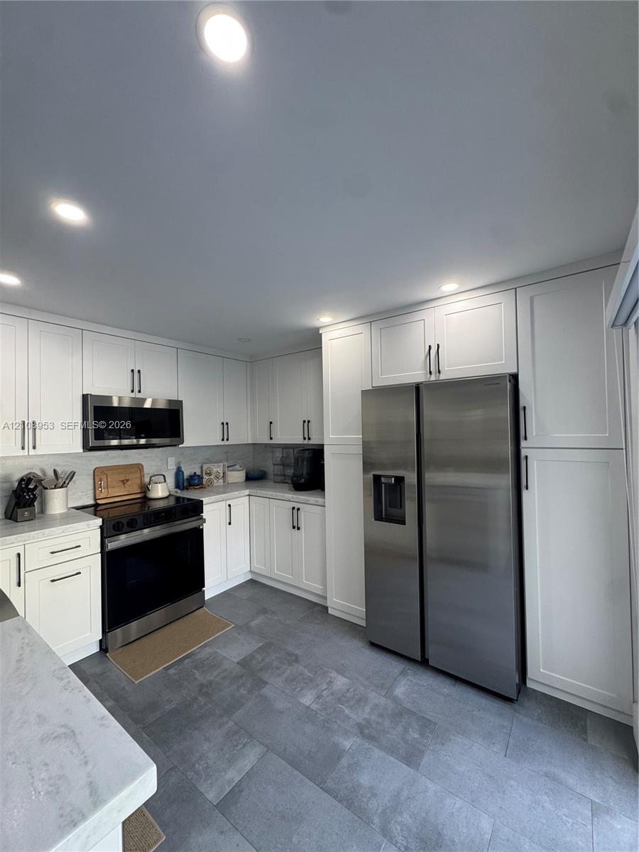 Kitchen featuring white shaker-style cabinetry, stainless steel appliances, stone-finish countertops, and large-format tile flooring