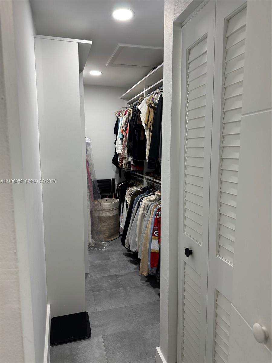 Walk-in storage space featuring ceramic tile flooring, built-in shelving, recessed lighting, and white louvered doors