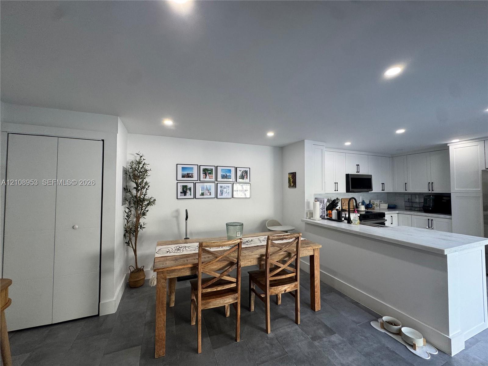 Kitchen featuring white shaker-style cabinetry, stone-finish countertops, matte black hardware, recessed ceiling lighting, and large-format tile flooring