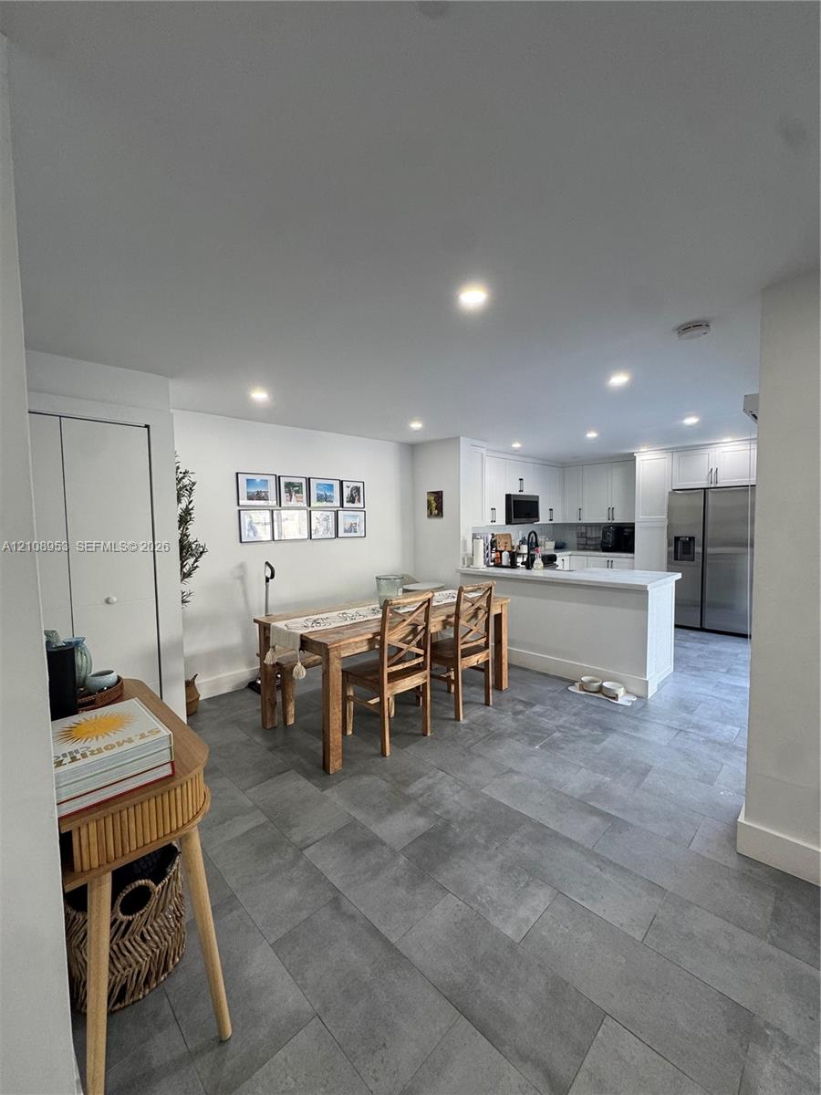 Kitchen featuring white shaker-style cabinetry, stainless steel appliances, and a breakfast bar peninsula, complemented by grey tile flooring and recessed lighting