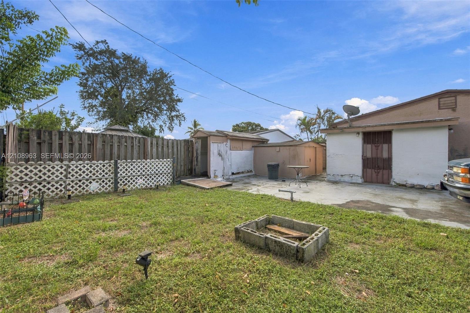 Rear yard featuring a concrete patio, perimeter wood fencing, decorative lattice paneling, and an exterior storage structure