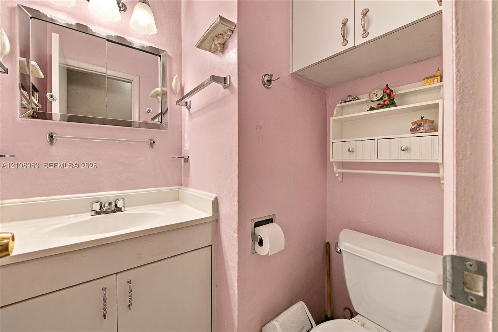 Bathroom featuring a vanity with integrated sink, rectangular framed mirror, upper cabinetry, and mounted storage shelving