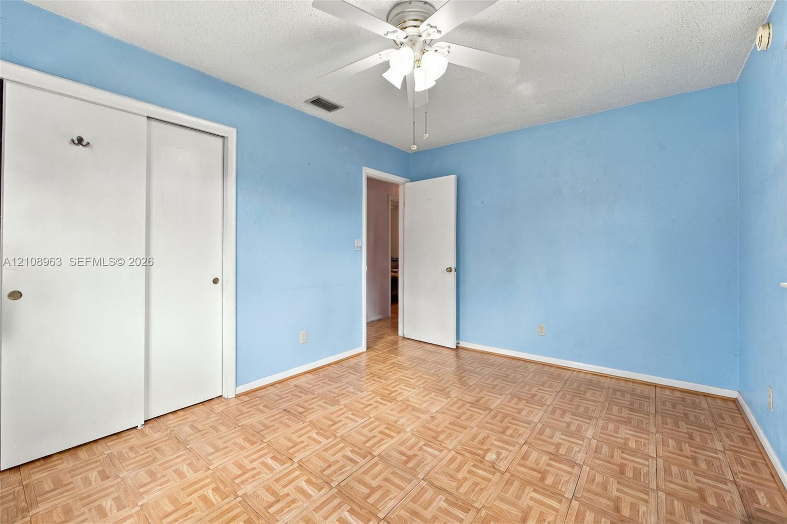Parquet wood-finish flooring, sliding closet doors, and ceiling-mounted light fixture with a fan