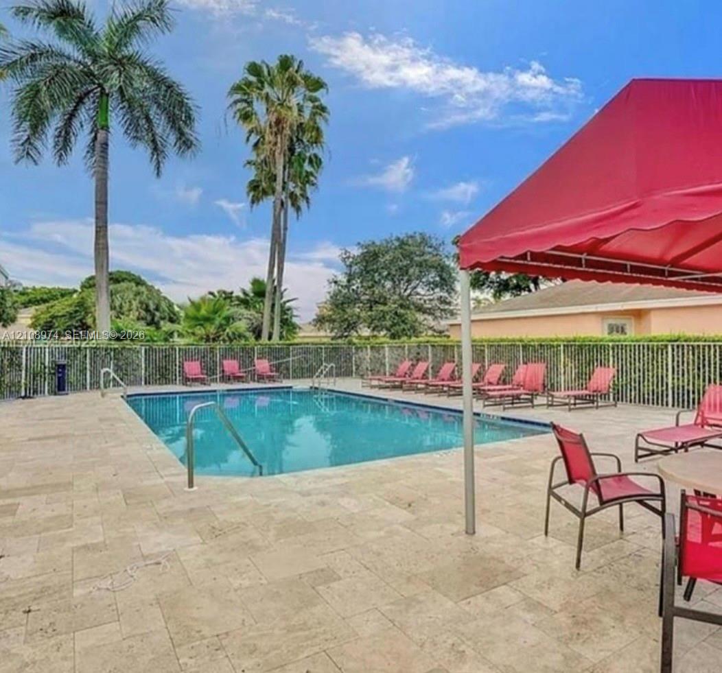 Outdoor swimming pool featuring a stone-paver deck, metal fencing, and mature palm trees