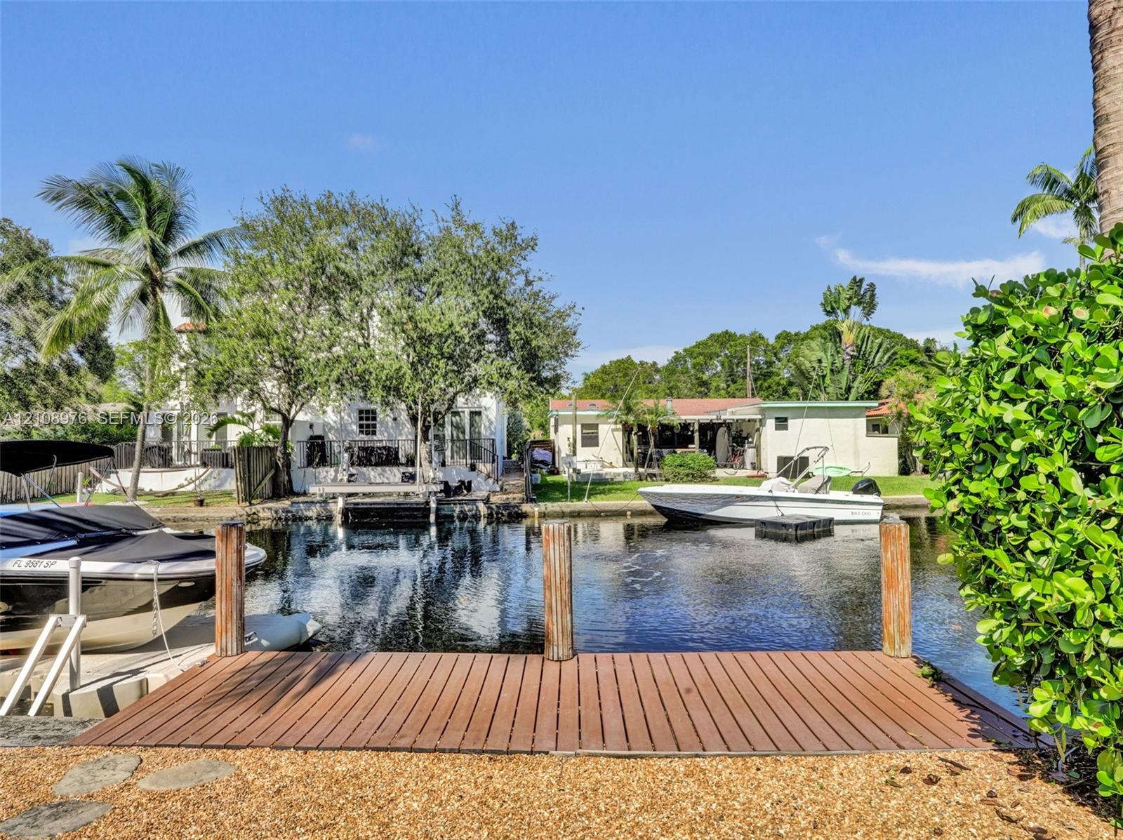 Waterfront canal property featuring a wooden boat dock, mature landscaping, and structural seawall