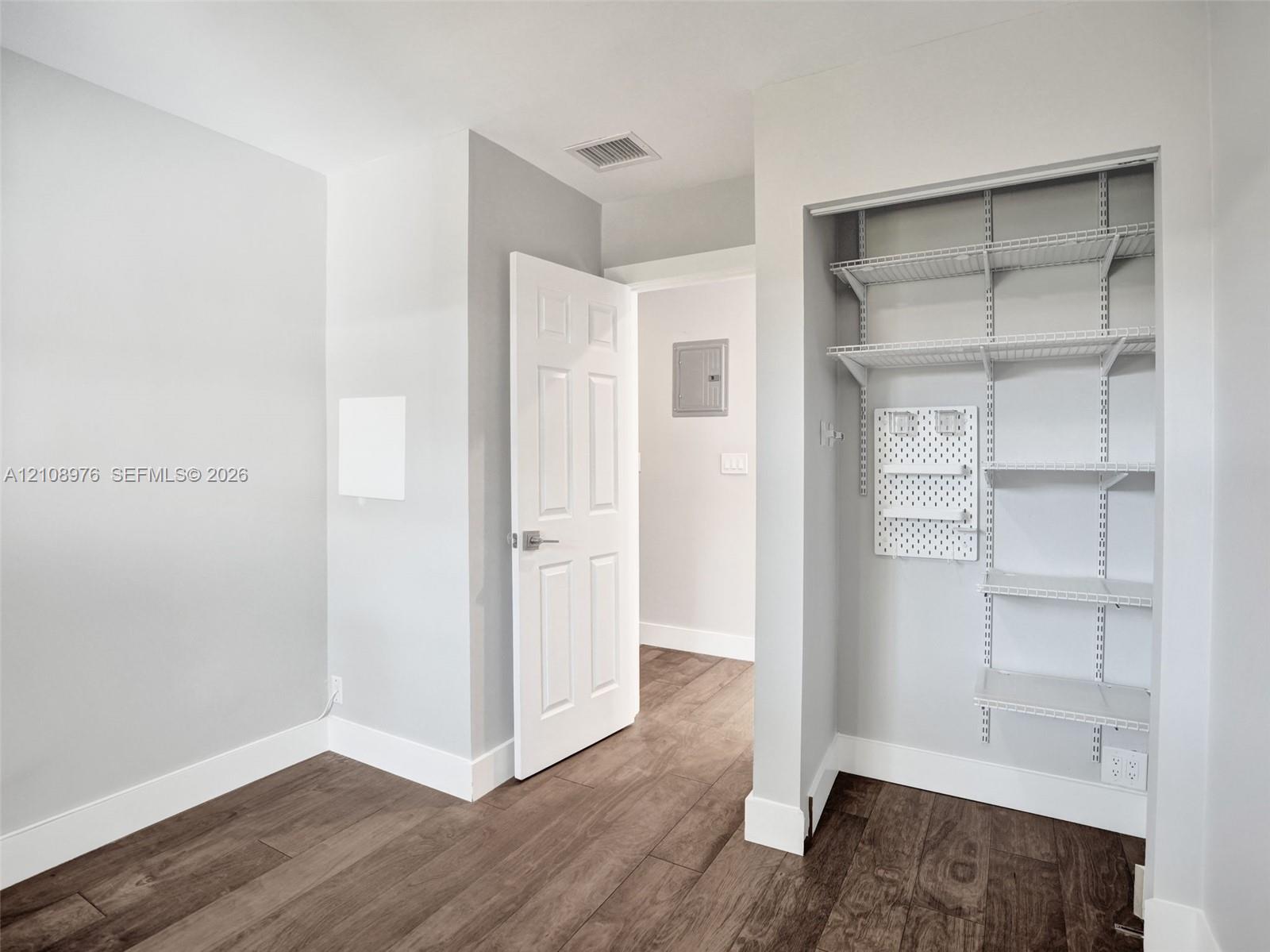Bedroom 3. Wood-finish flooring featuring a built-in closet with adjustable wire shelving and a wall-mounted pegboard organizer