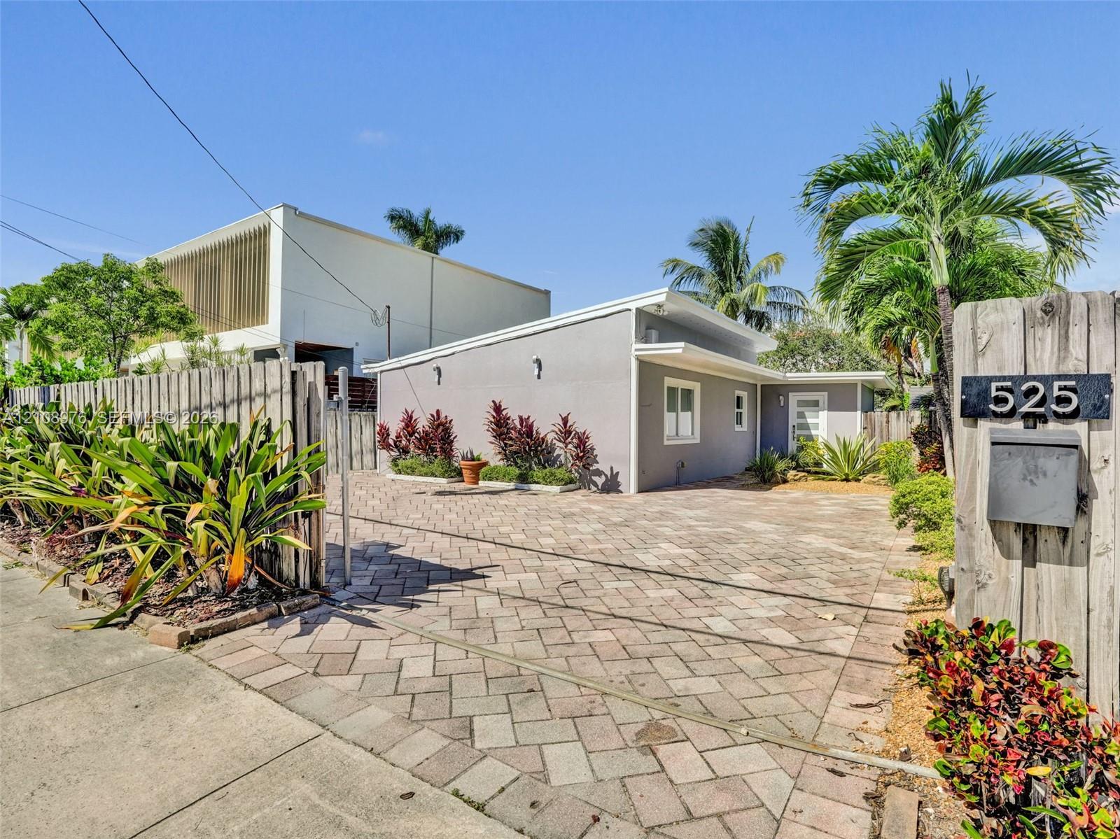 Single-story residence featuring a paved brick driveway, low-slope roofline, light-toned exterior finish, and fenced perimeter