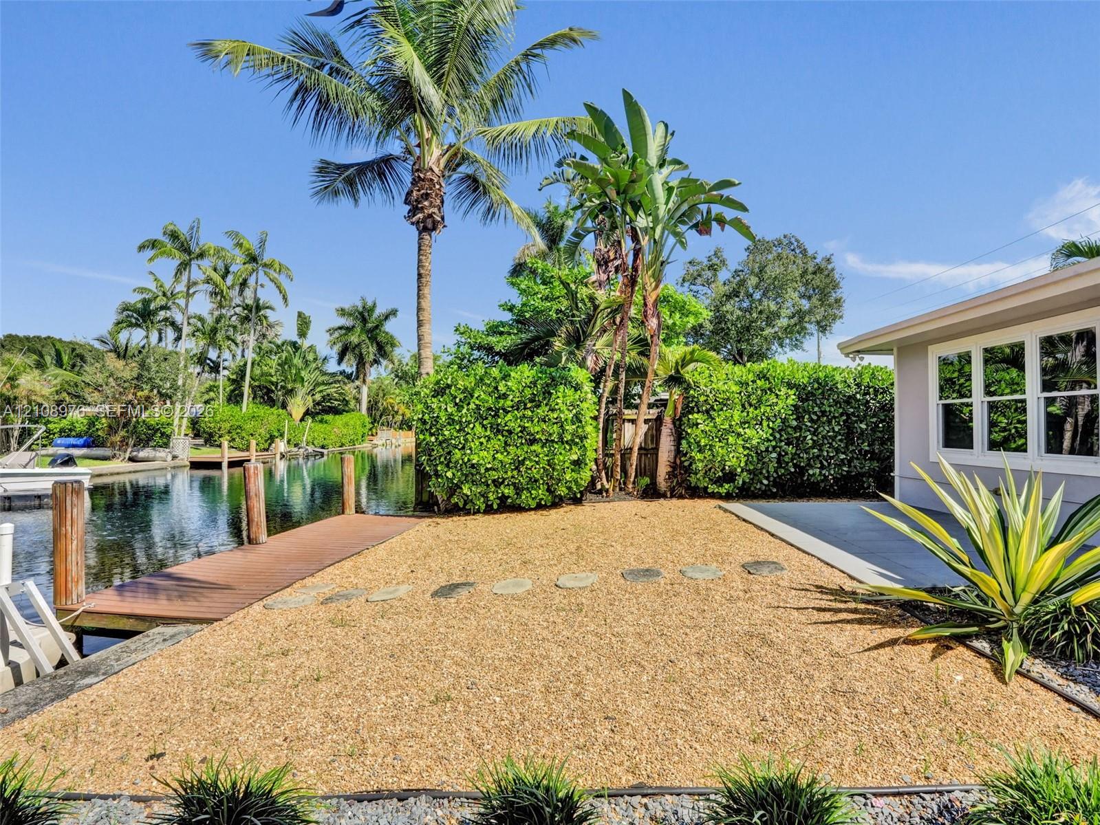 Waterfront property featuring a private dock, graveled outdoor space, concrete patio, and mature landscaping