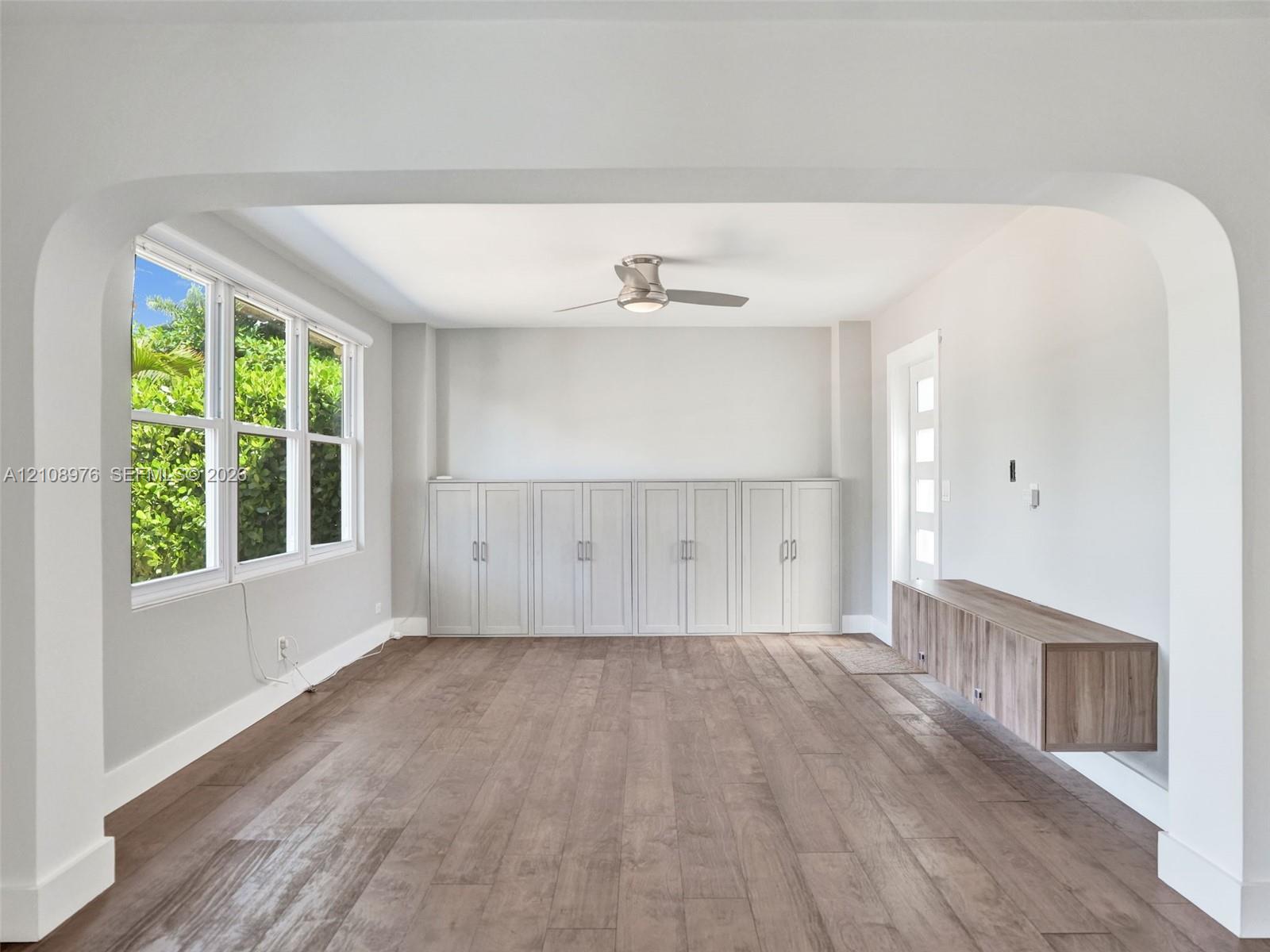 Architectural archway, wood-finish flooring, full-wall built-in cabinetry, wall-mounted floating console, and ceiling fan with integrated lighting