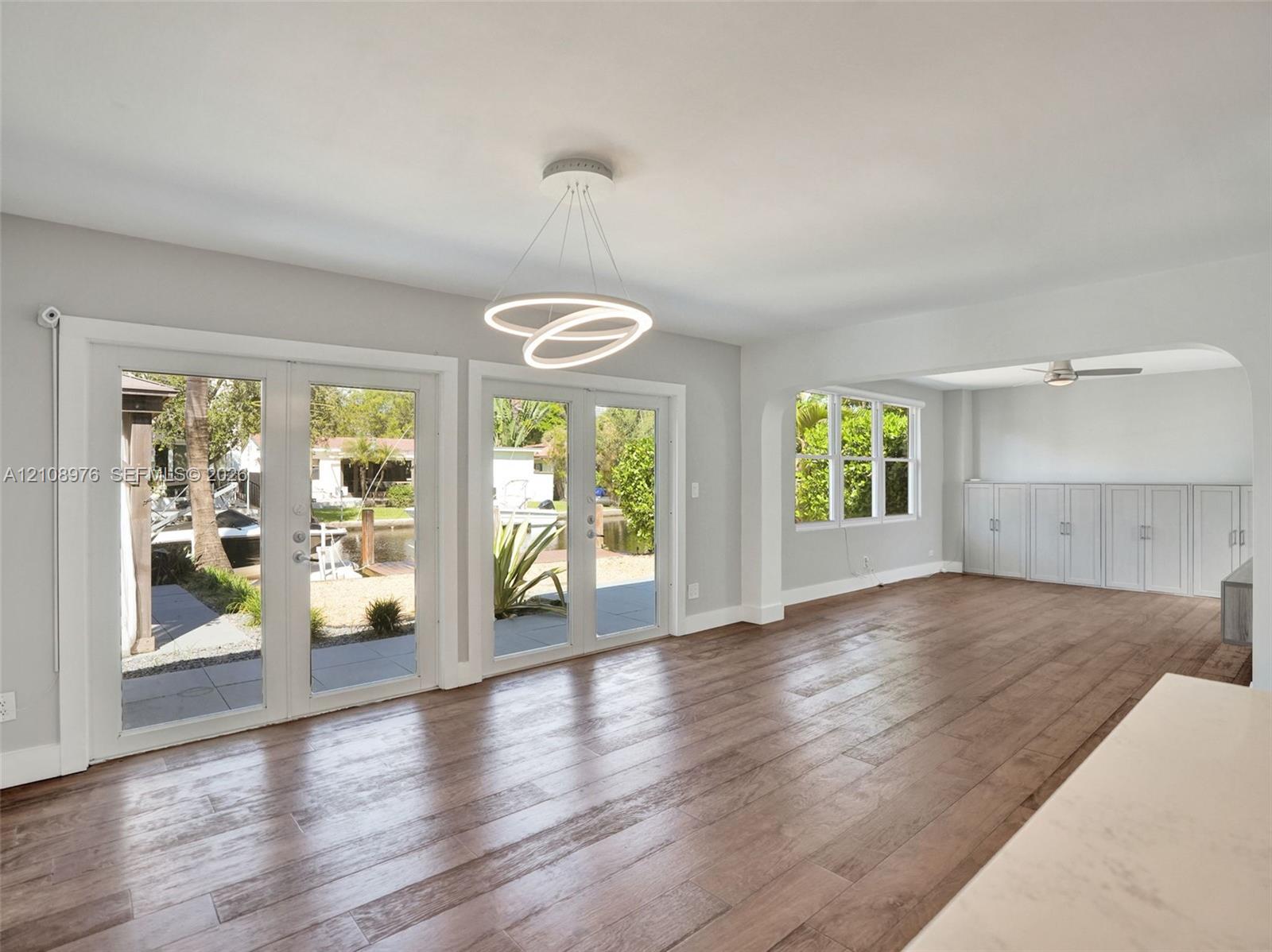 Living space featuring wood-finish flooring, dual sets of French doors, an integrated circular LED light fixture, and custom built-in cabinetry with an arched room partition