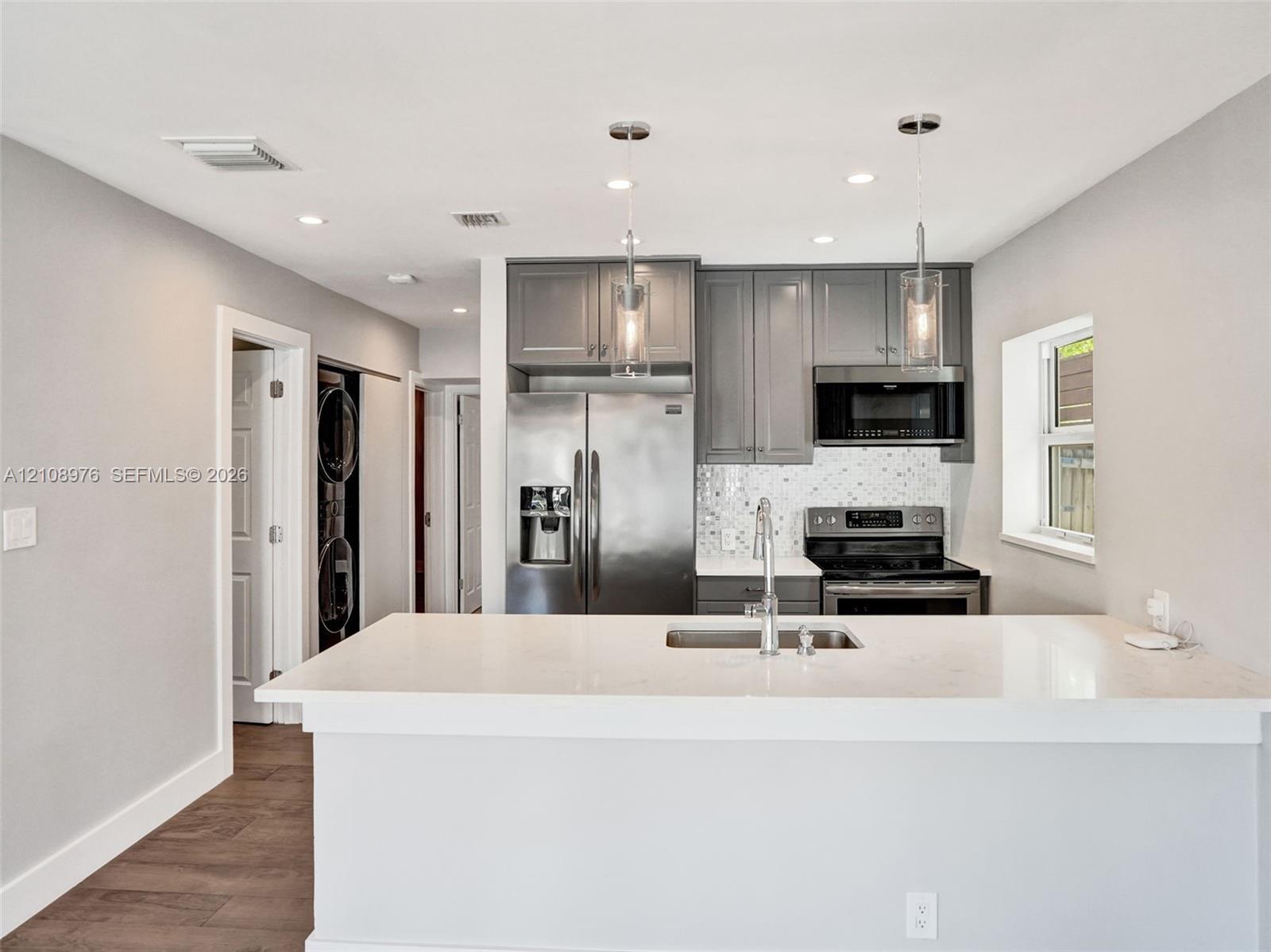 Kitchen featuring gray cabinetry, stainless steel appliances, white quartz countertops, mosaic tile backsplash, and dual pendant lighting