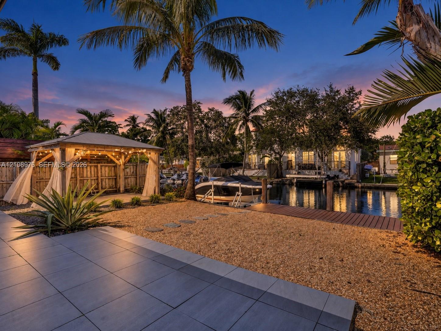 Waterfront property featuring a covered timber-framed gazebo, wooden dock, gravel landscaping, and large-format tile patio Waterfront property featuring a covered timber-framed gazebo, wooden dock, gravel landscaping, and large-format tile patio
