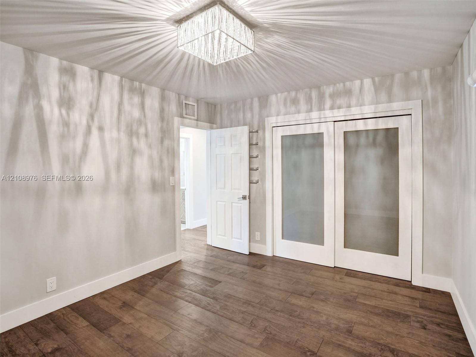 Wood-finish flooring featuring a square, multi-faceted crystal ceiling fixture, dual-panel sliding doors with frosted glass inserts, and a six-panel interior door