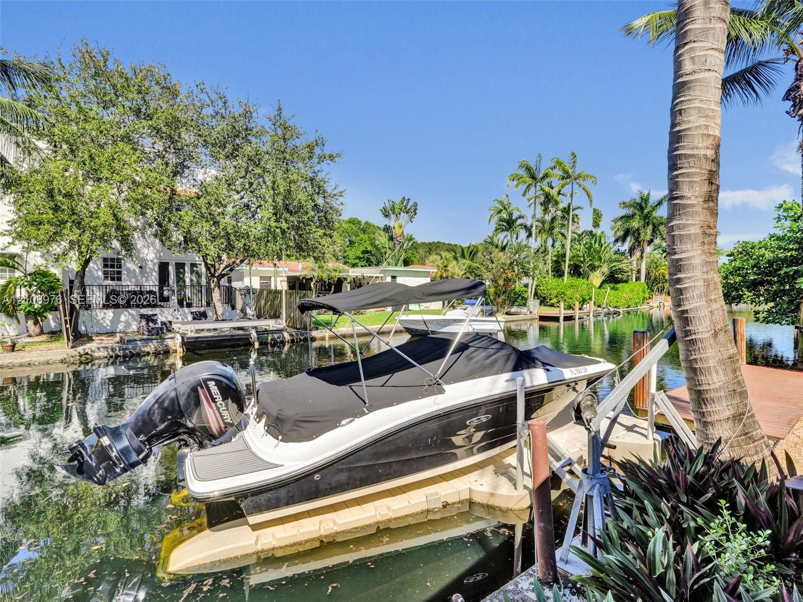 Waterfront bulkhead featuring a boat lift, concrete seawall, and tropical landscaping