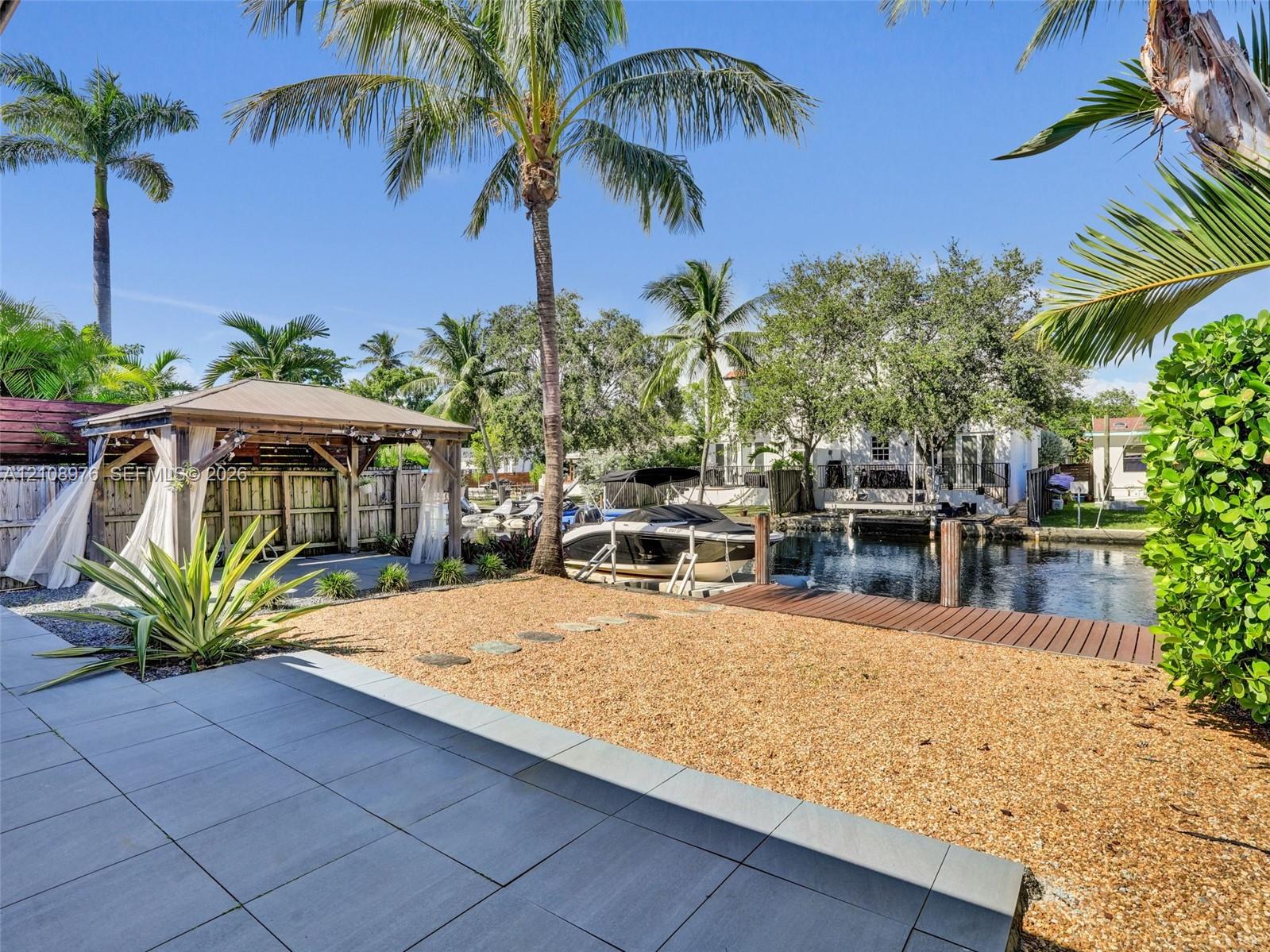Waterfront grounds featuring a permanent timber-frame gazebo, with space for a summer kitchen and living are, a private dock, gravel hardscaping, and large-format porcelain patio tiling