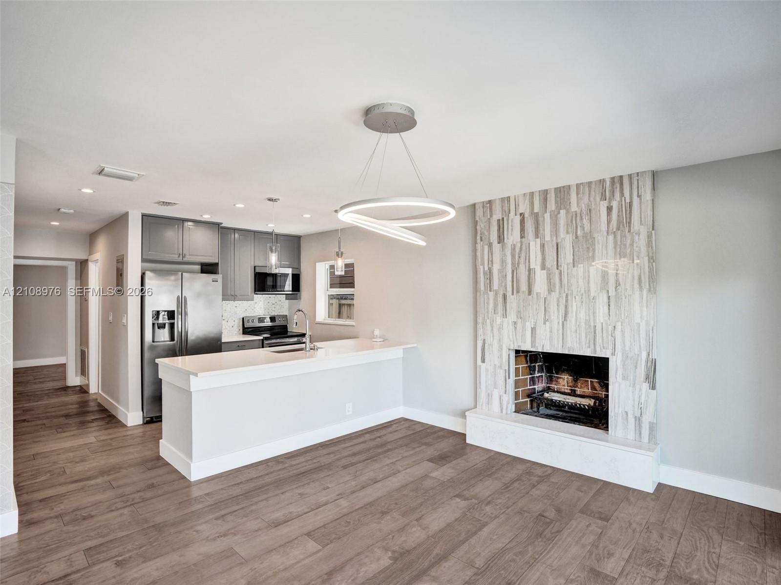 Open concept interior featuring wood-finish flooring, a kitchen with quartz countertops and stainless steel appliances, and a floor-to-ceiling textured stone fireplace surround