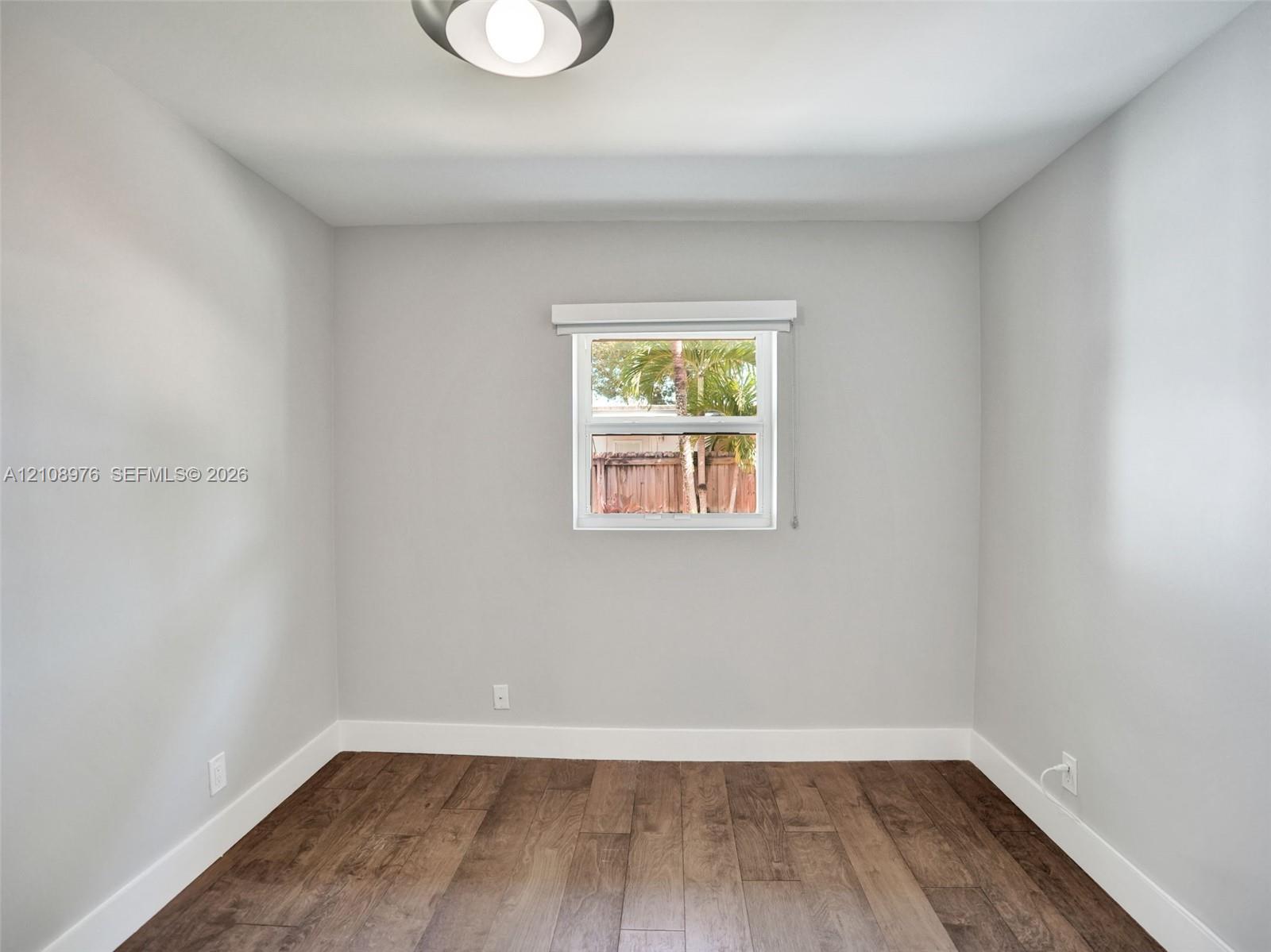 Bedroom 3. Neutral wall paint, wood-finish flooring, and single-pane window with installed window treatment, complemented by a flush-mount ceiling fixture