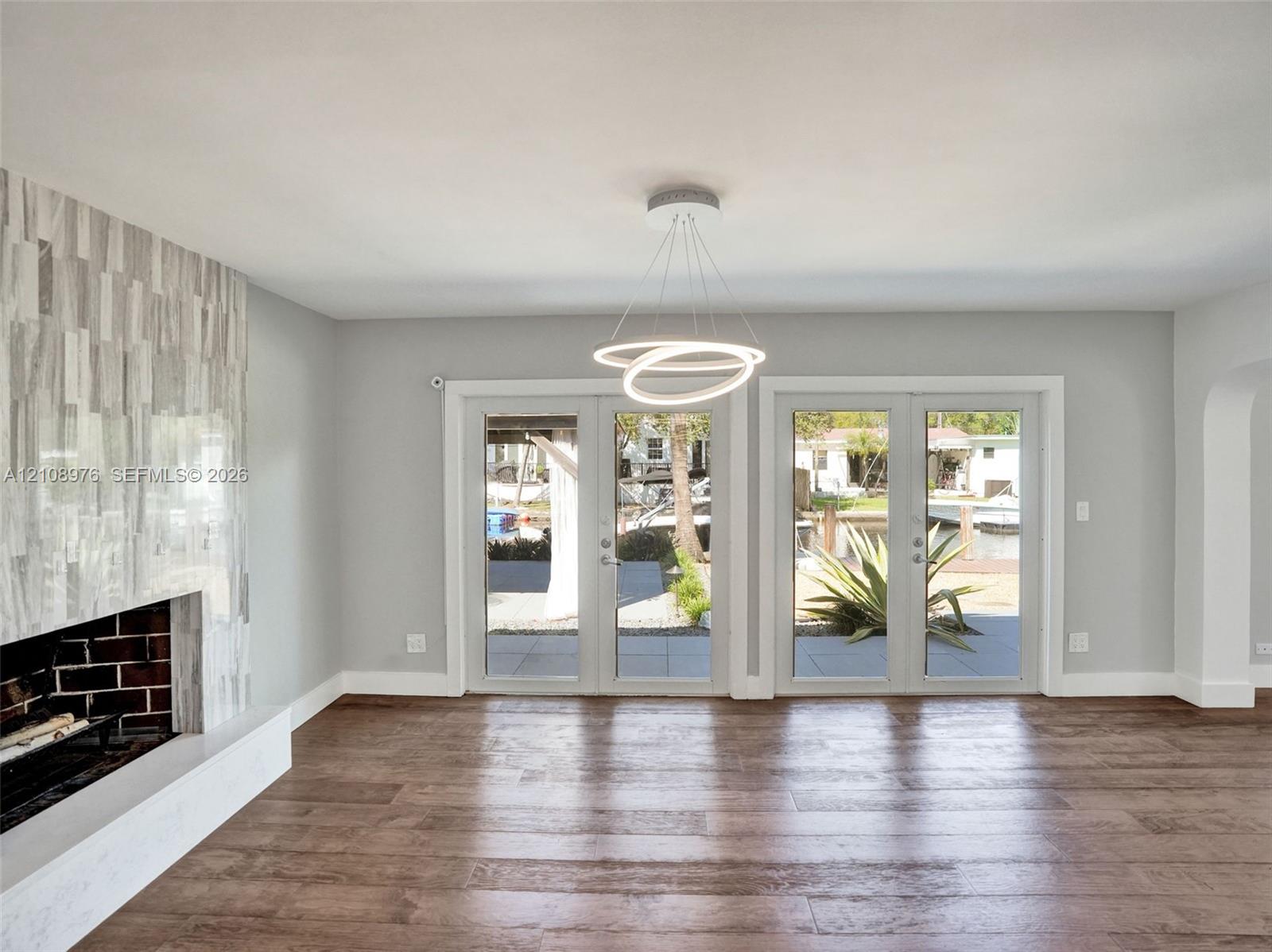Living area featuring wood-finish flooring, a contemporary circular pendant light fixture, and dual sets of glass-paned doors