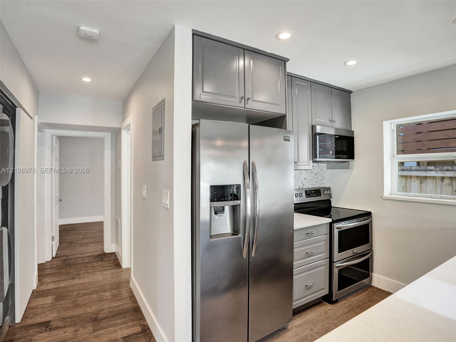 Kitchen featuring grey shaker-style cabinetry, stainless steel side-by-side refrigerator, double wall oven, quartz countertops, and recessed lighting