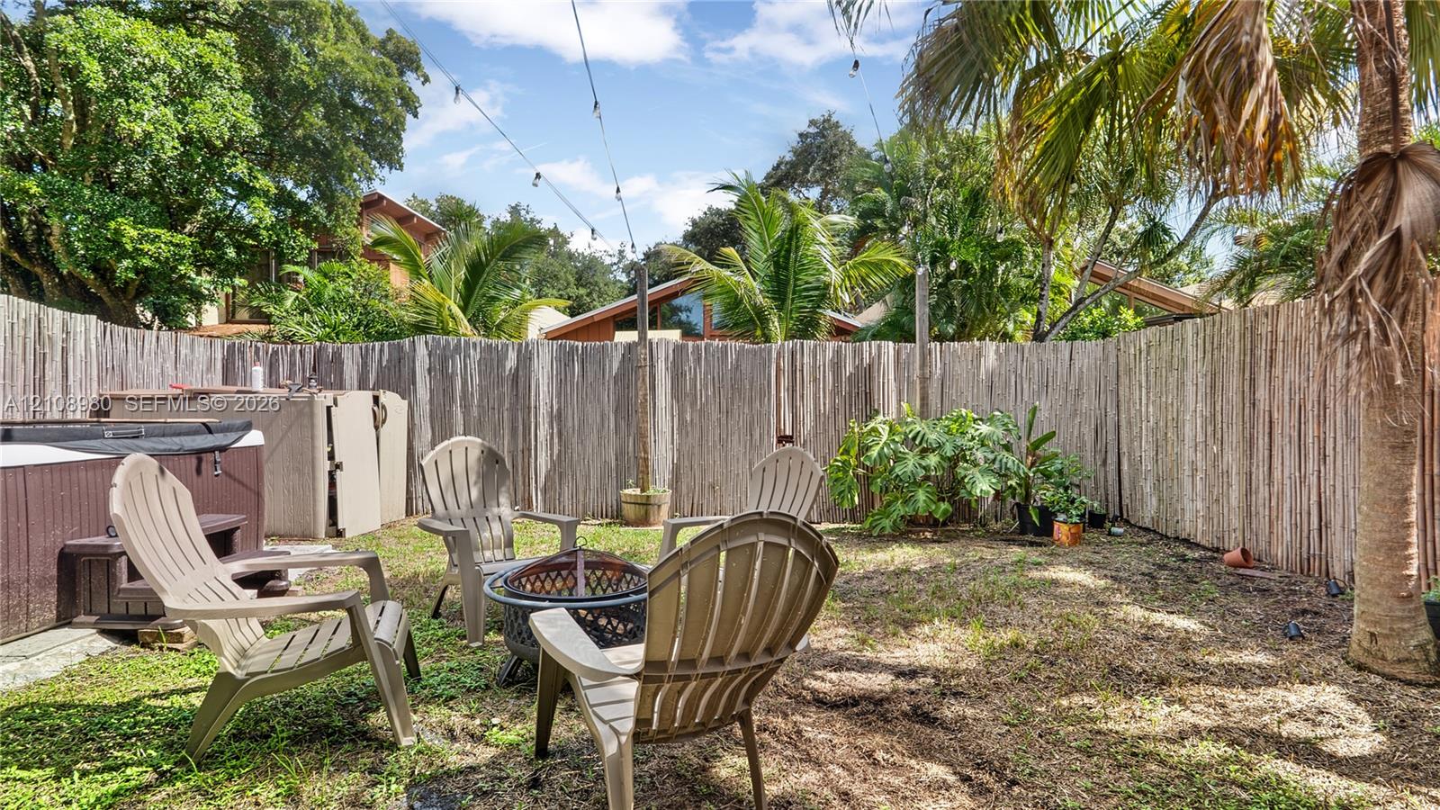 Backyard area featuring a built-in jetted spa, organic material perimeter fencing, string lighting, and mature palm trees