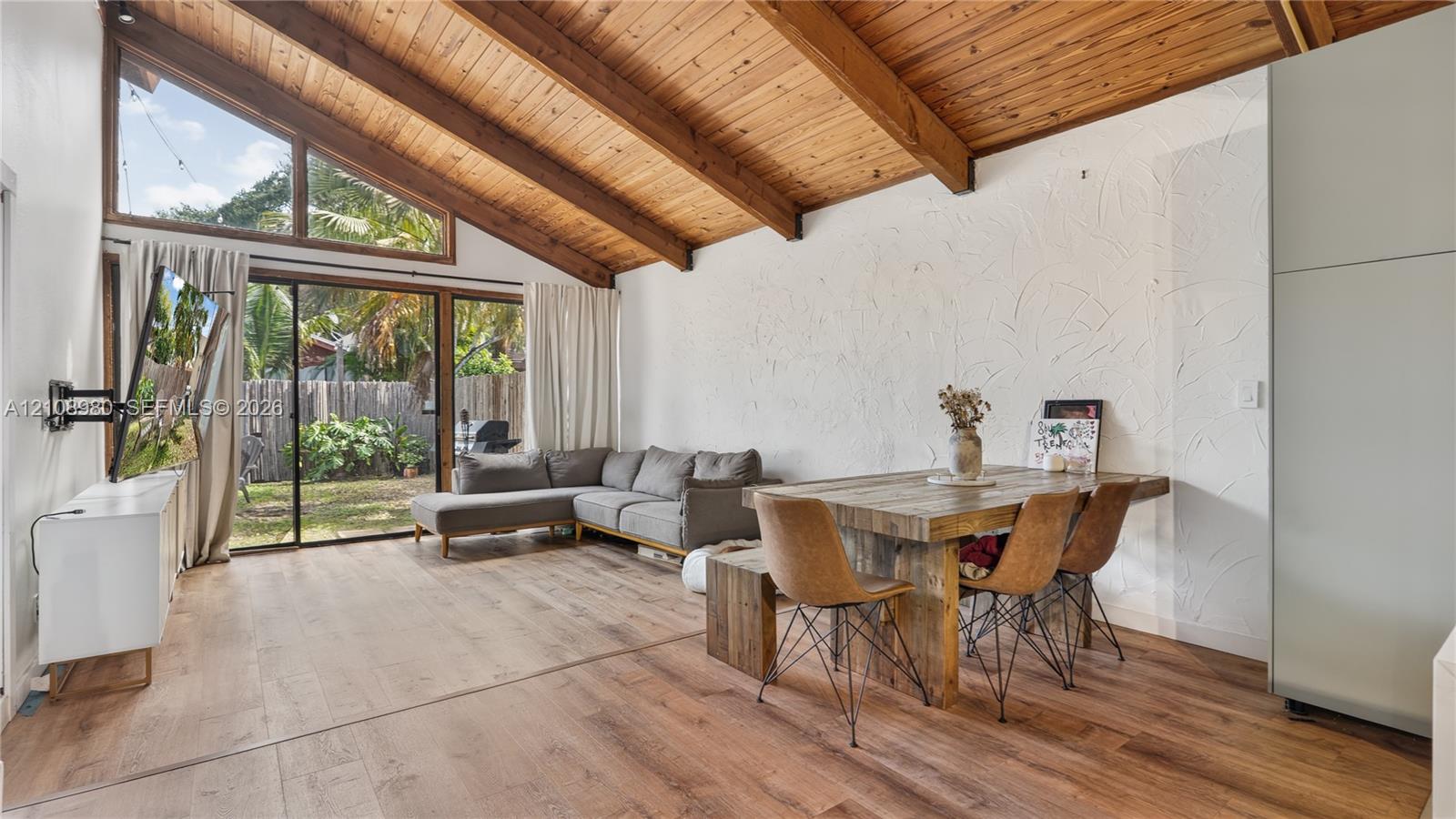 Vaulted wood-plank ceiling featuring exposed beams, wood-finish flooring, texturized wall finish, and floor-to-ceiling glass sliding doors with clerestory windows