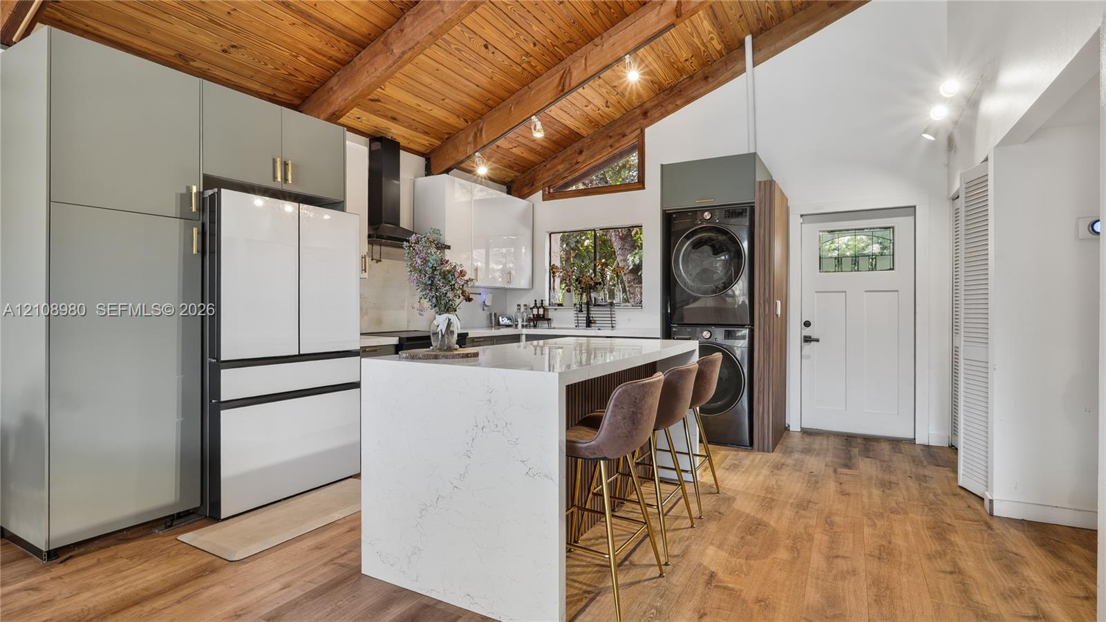 Kitchen featuring a vaulted ceiling with exposed wood beams, center island with stone-finish countertop, flat-panel cabinetry, and integrated laundry appliances