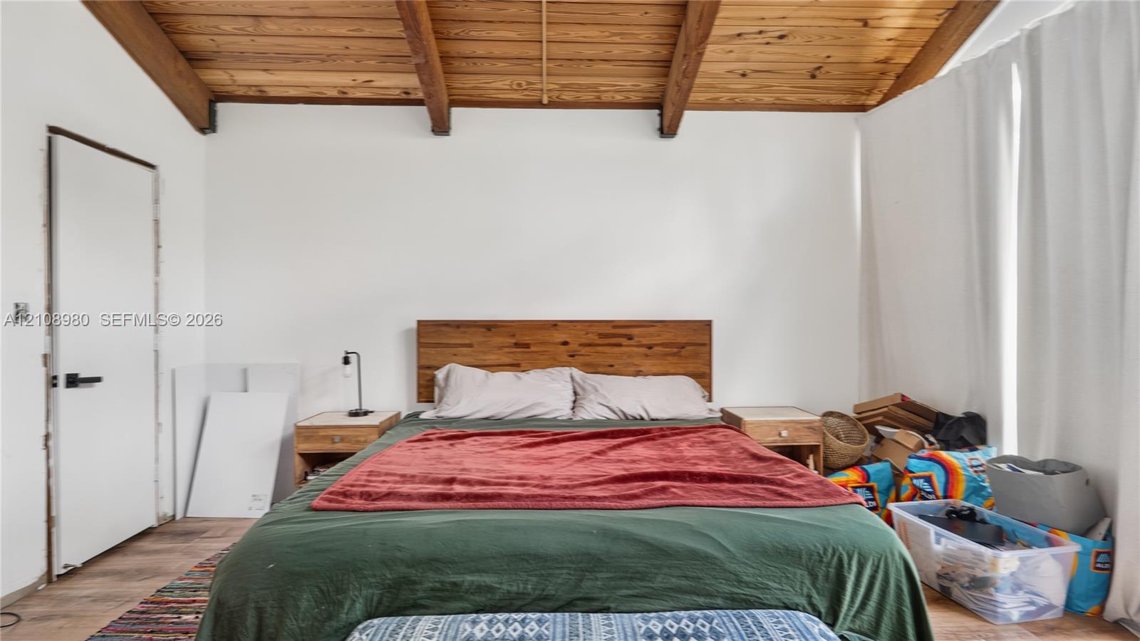 Vaulted ceiling featuring exposed wood beams, wood-finish flooring, and a flat-panel interior door with matte black hardware