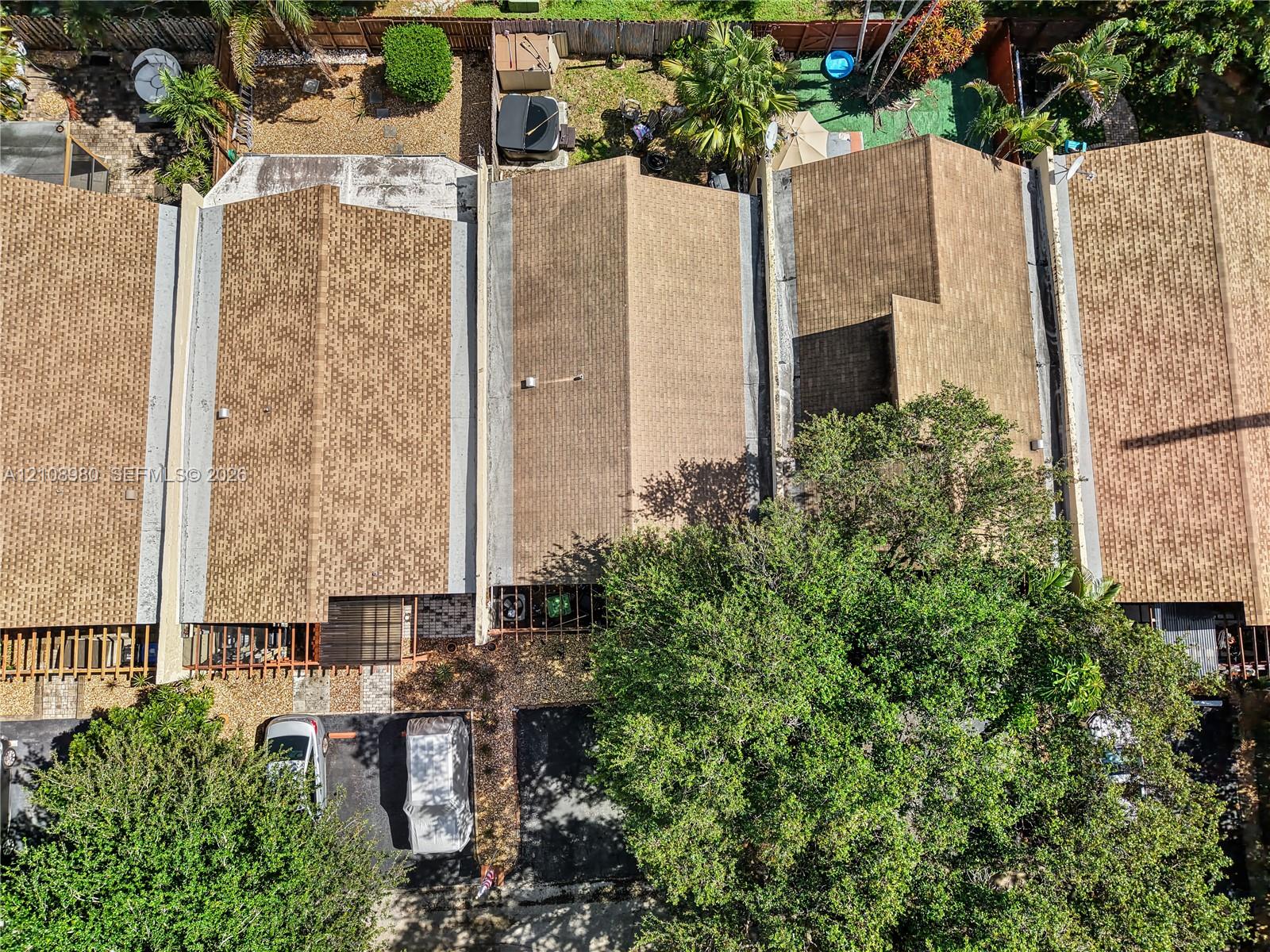 Aerial perspective featuring asphalt shingle roofing, paved surface parking, and mature canopy trees