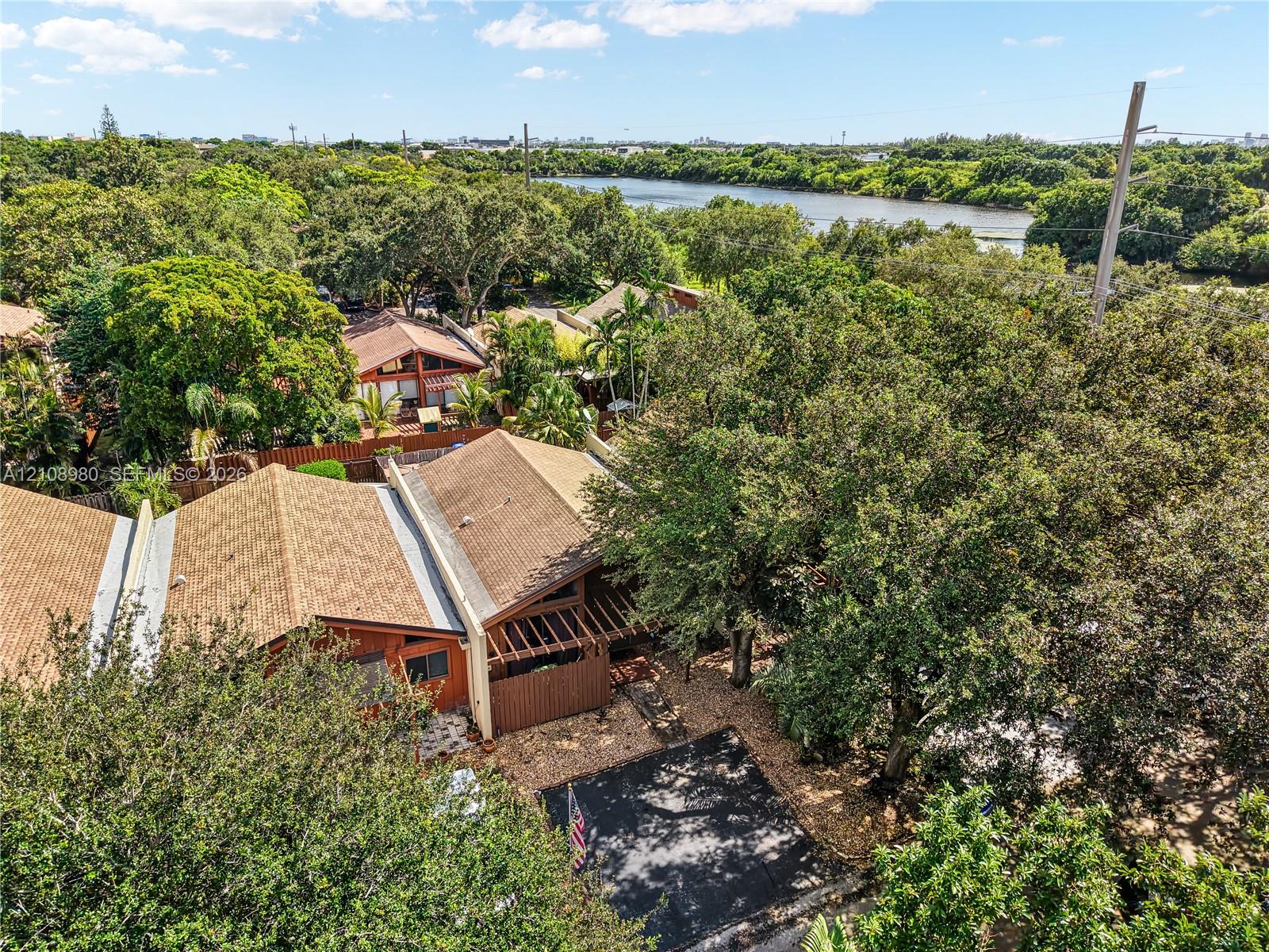 Aerial perspective of a multi-unit property featuring wood-toned shingle roofing, integrated wood-slat privacy fencing, paved driveways, and mature oak canopy within a waterfront setting