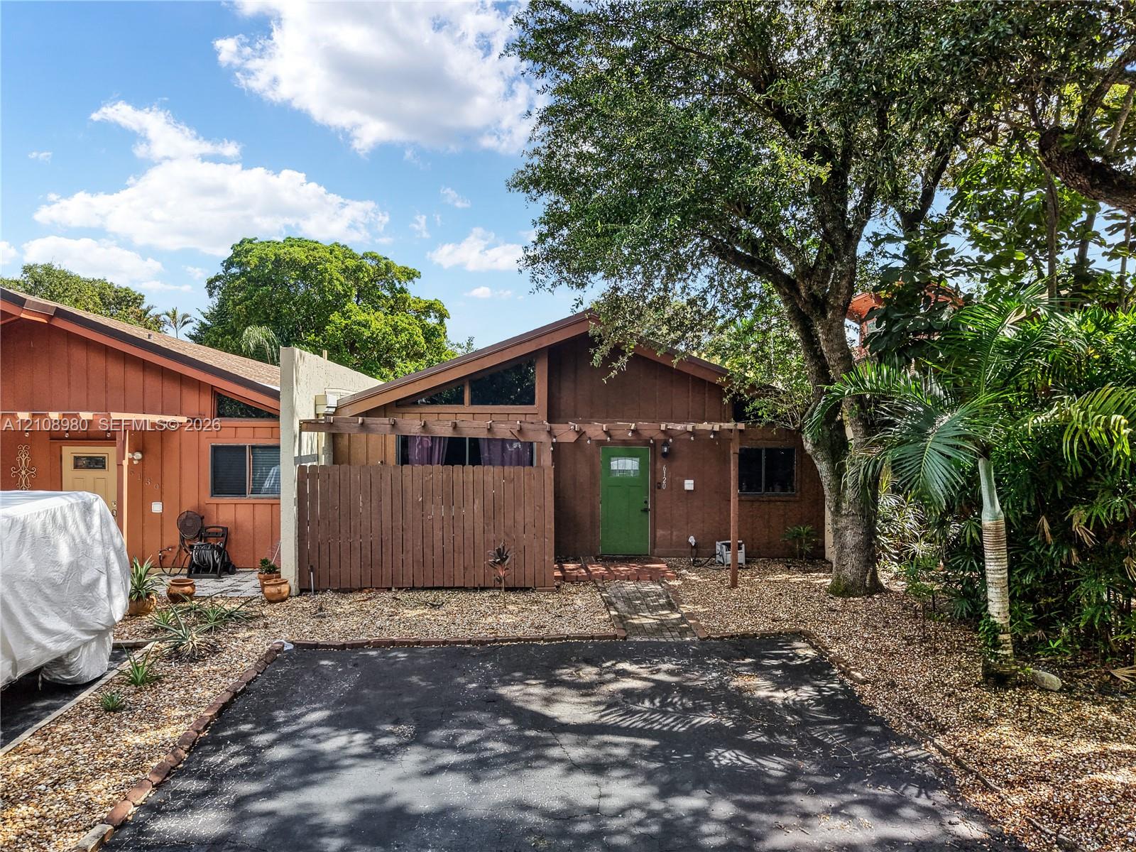 Single-story exterior with wood-style siding, pitched roofline, attached wooden pergola, and gravel landscaping
