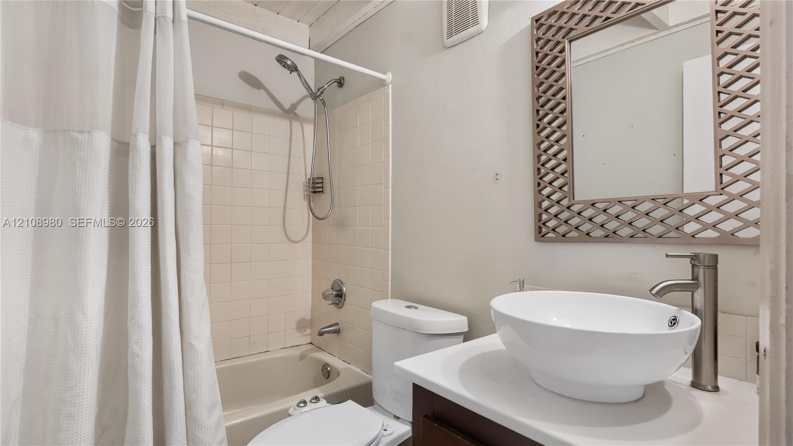 Bathroom featuring a vanity with a white vessel sink, a tall metallic faucet, a tiled shower-tub combination with a handheld showerhead, and a framed mirror