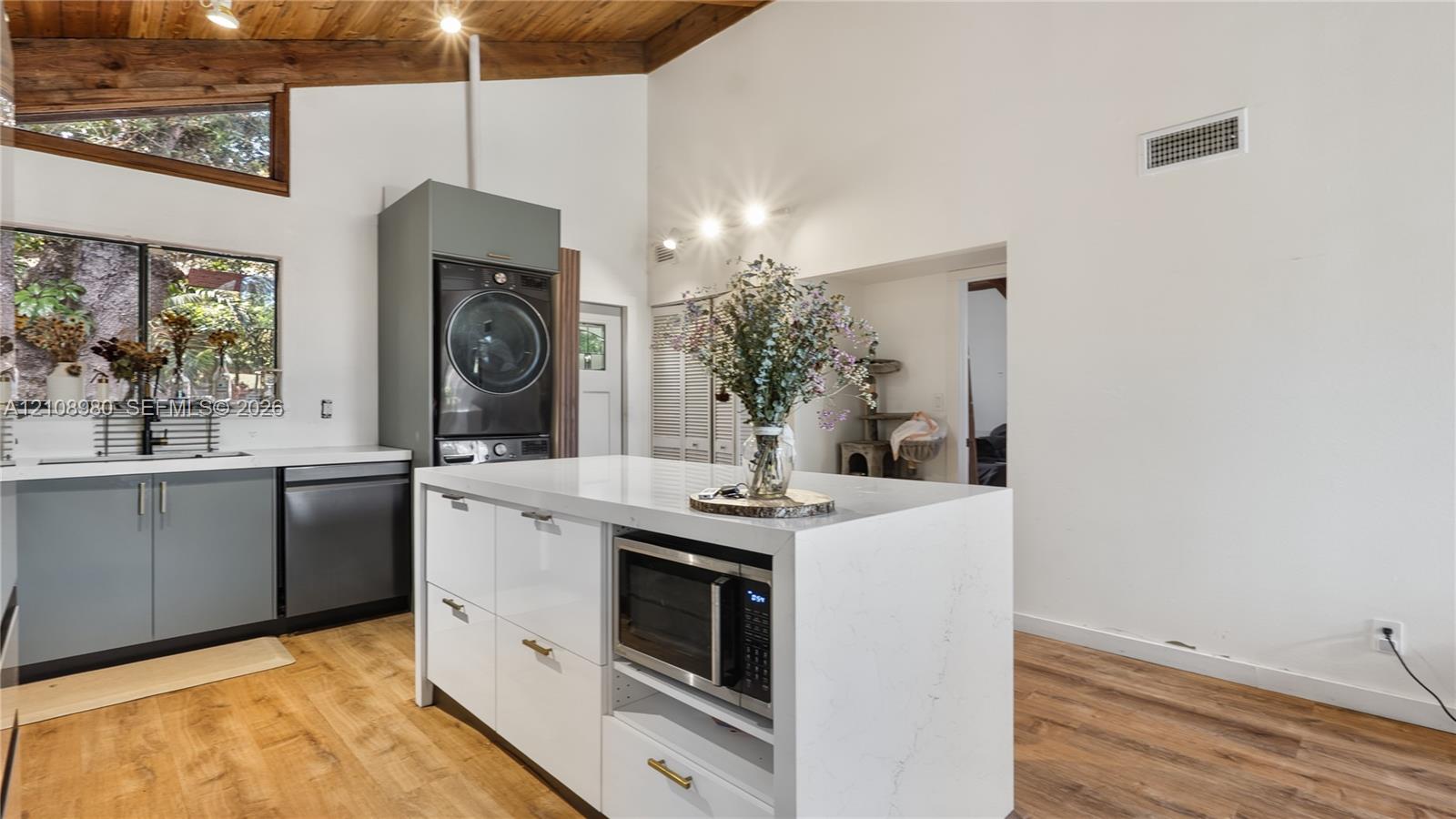 Vaulted ceiling featuring exposed wood beams, center island with stone-surface countertop, wood-finish flooring, matte-finish cabinetry, and stainless steel built-in appliances