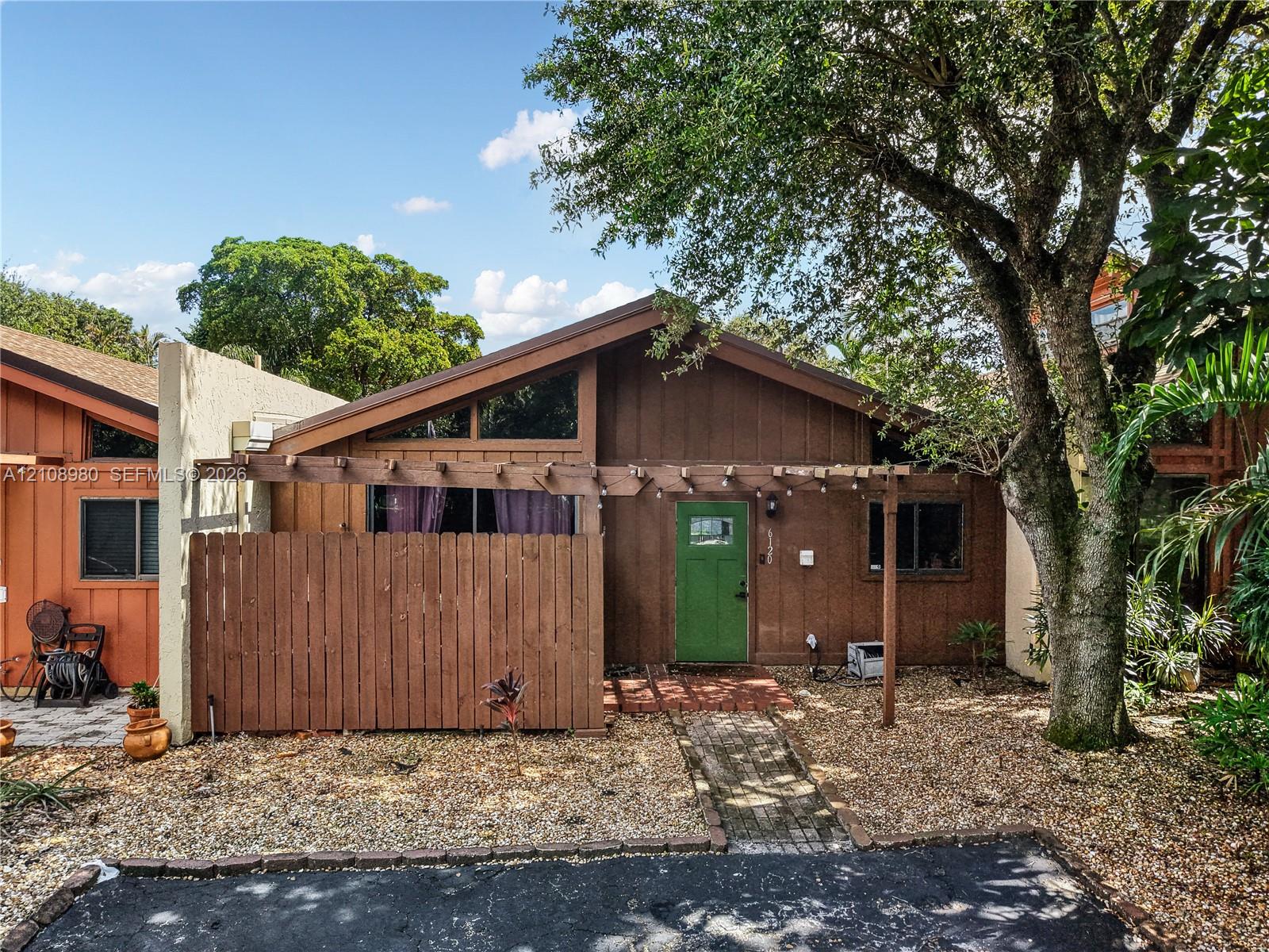 Exterior featuring a gabled roofline, wood-paneled siding, a decorative timber pergola, and a brick-paved entry path